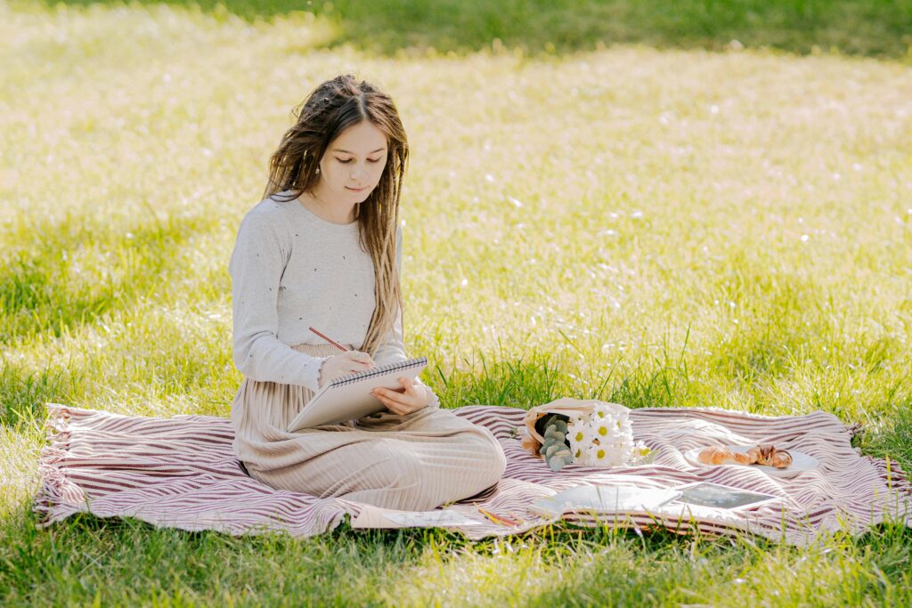 Woman sitting on a blanket reading a book in a field.