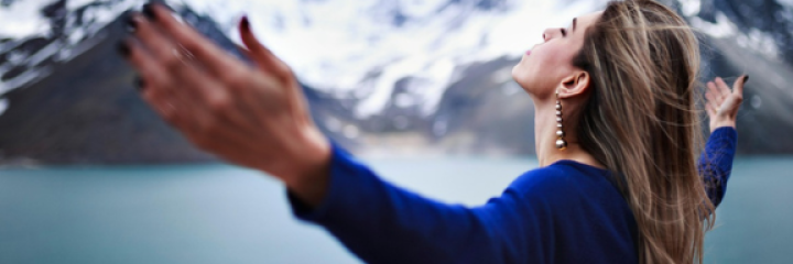 Woman with hands outstretched Woman holding her hands apart in front of Lake and mountains with snow caps.